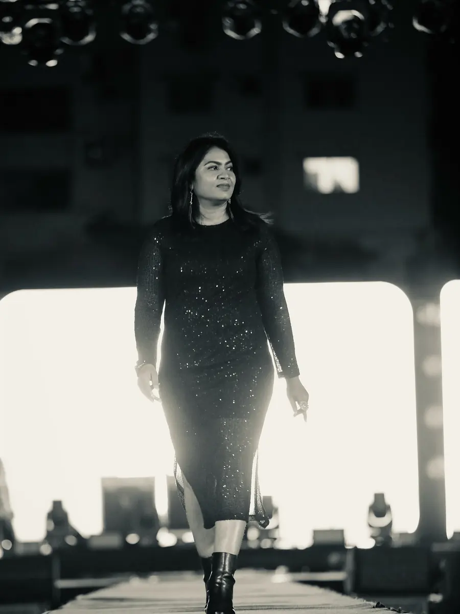 VJ Reena walking down a stage runway in a sequinned dress, stage lights glowing behind her
